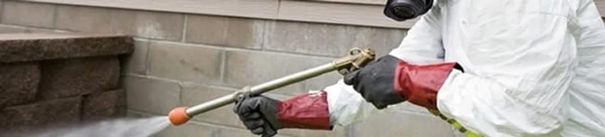 Pest control technician applying exterior insect treatment along a home foundation in South Bend, IN