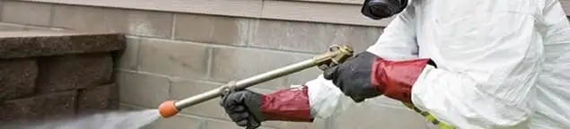 Pest control technician applying exterior insect treatment along a home foundation in South Bend, IN