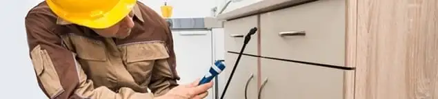 Roach exterminator applying treatment under kitchen cabinets in South Bend, IN