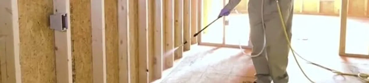 Termite treatment technician applying spray along framing and unfinished walls in South Bend, IN