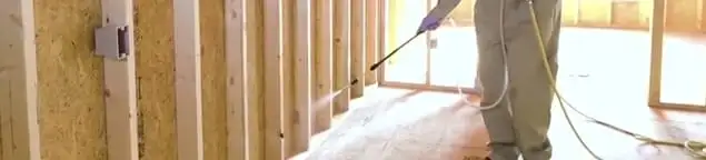 Termite treatment technician applying spray along framing and unfinished walls in South Bend, IN